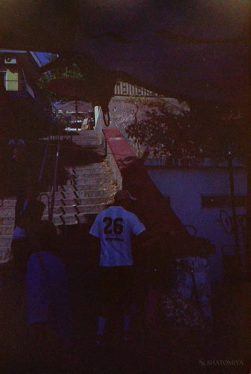 Man wearing a football shirt, stands in front of stairs in a crowded neighborhood during the flea market and carries a trailer with garlic.